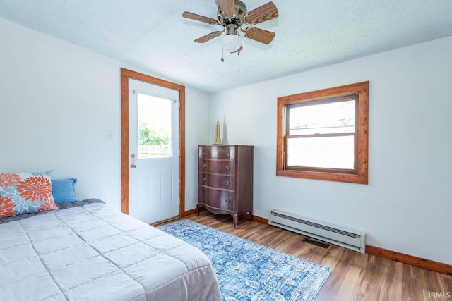 bedroom featuring baseboard heating, baseboards, multiple windows, and a textured ceiling