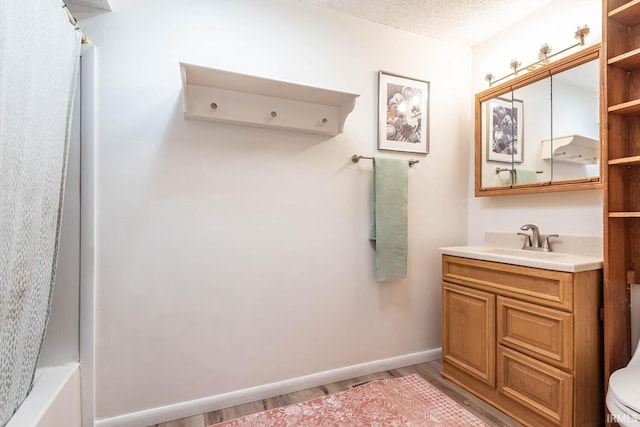 full bathroom with wood finished floors, vanity, toilet, baseboards, and a textured ceiling