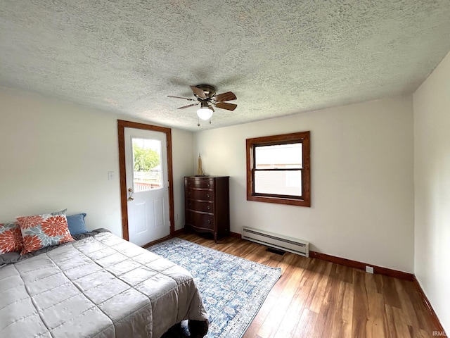 bedroom featuring a baseboard heating unit, baseboards, wood finished floors, a ceiling fan, and a textured ceiling
