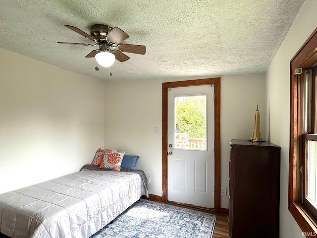 bedroom with a textured ceiling, a ceiling fan, wood finished floors, and baseboards