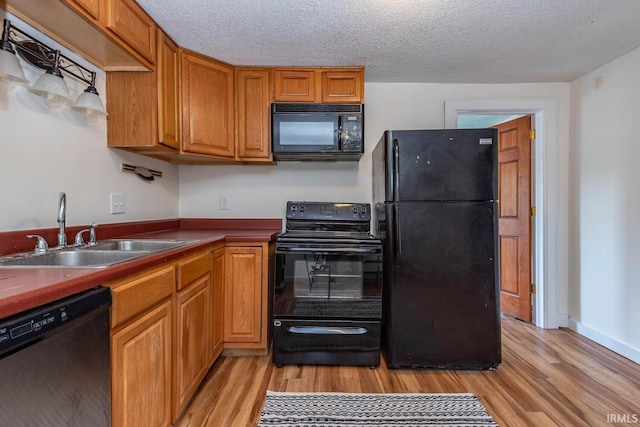 kitchen with black appliances, a sink, light wood-style floors, brown cabinets, and a textured ceiling