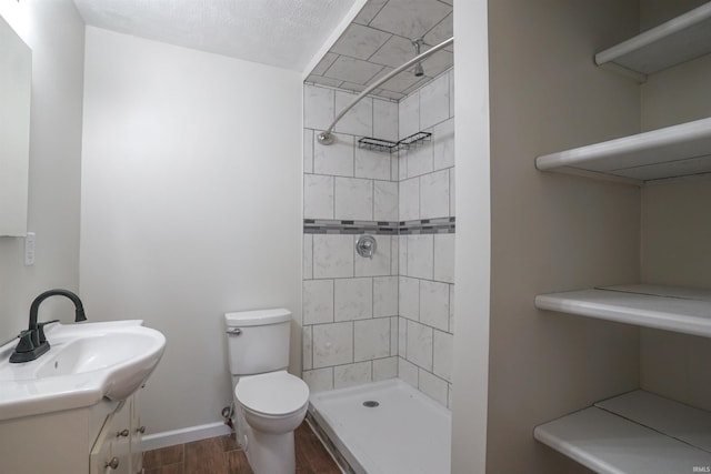 bathroom with baseboards, toilet, wood finished floors, vanity, and tiled shower