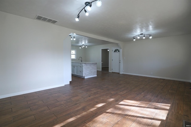 empty room featuring track lighting, a sink, baseboards, visible vents, and dark wood-type flooring
