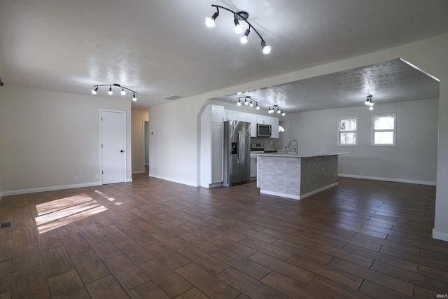 unfurnished living room featuring a sink, visible vents, baseboards, dark wood-style flooring, and track lighting