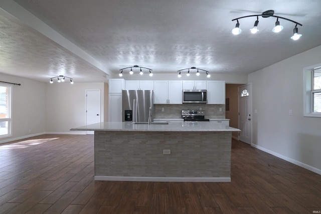 kitchen with white cabinetry, appliances with stainless steel finishes, baseboards, dark wood-style floors, and a center island with sink