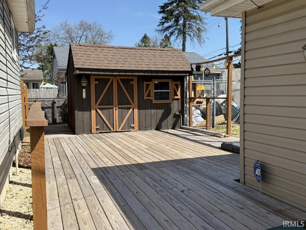 wooden terrace with a storage unit, fence, and an outdoor structure