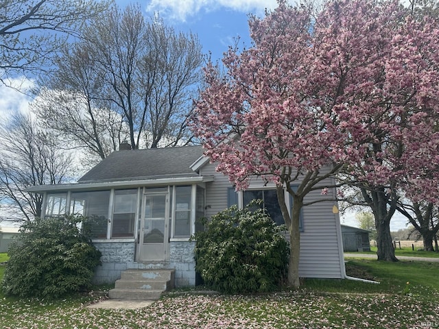 view of front of house featuring a chimney, entry steps, a sunroom, roof with shingles, and a front lawn