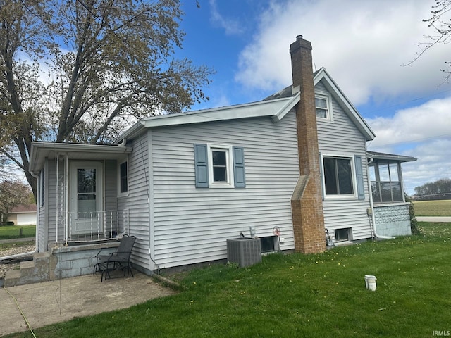 back of property featuring a lawn, a chimney, cooling unit, and a sunroom