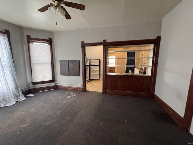 carpeted spare room with a healthy amount of sunlight, a ceiling fan, and baseboards