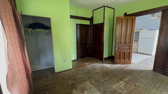 unfurnished bedroom featuring a closet, hardwood / wood-style flooring, freestanding refrigerator, and baseboards