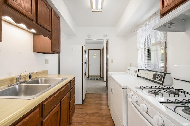 kitchen with wood finished floors, white appliances, light countertops, under cabinet range hood, and a sink