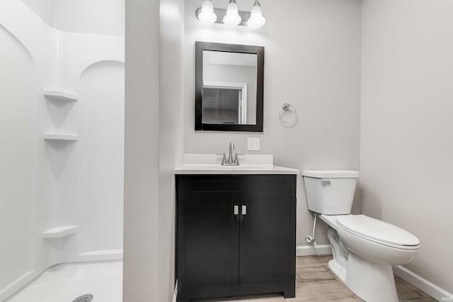 bathroom with wood finished floors, walk in shower, toilet, vanity, and baseboards