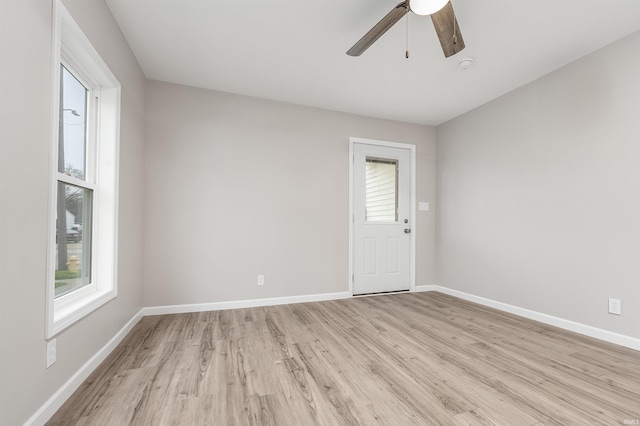 spare room with light wood-type flooring, a ceiling fan, and baseboards