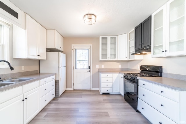kitchen featuring a sink, light wood-style floors, freestanding refrigerator, under cabinet range hood, and black range with gas cooktop