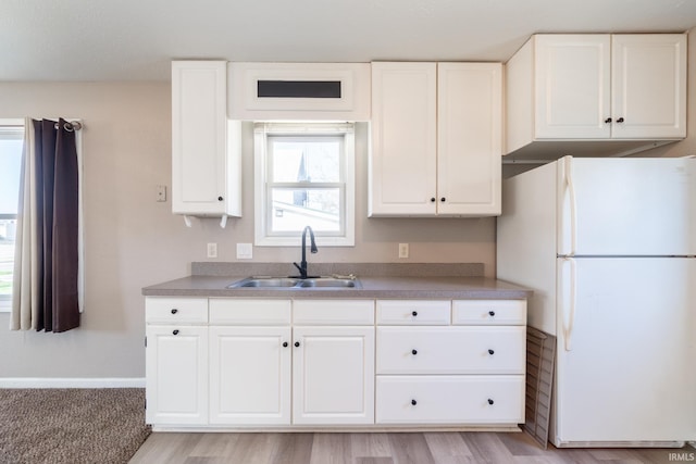 kitchen with white cabinetry, freestanding refrigerator, and a sink