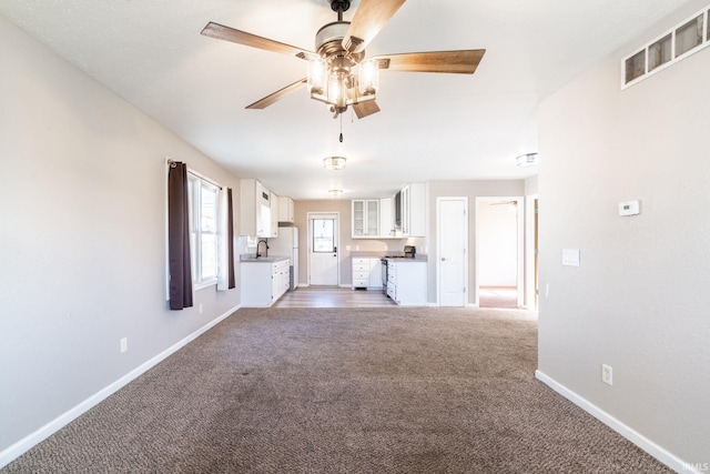 unfurnished living room featuring baseboards, visible vents, light carpet, and ceiling fan