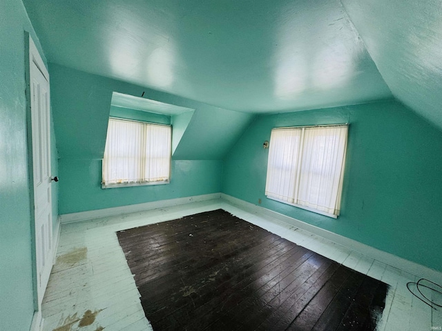 additional living space with lofted ceiling, a wealth of natural light, baseboards, and wood-type flooring