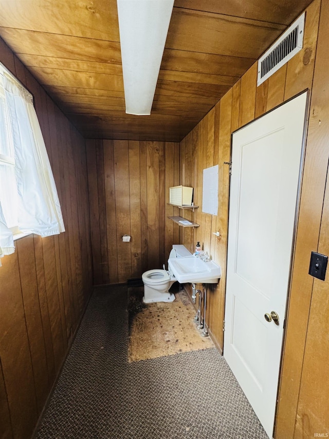 half bath featuring wooden ceiling, a sink, toilet, wooden walls, and visible vents