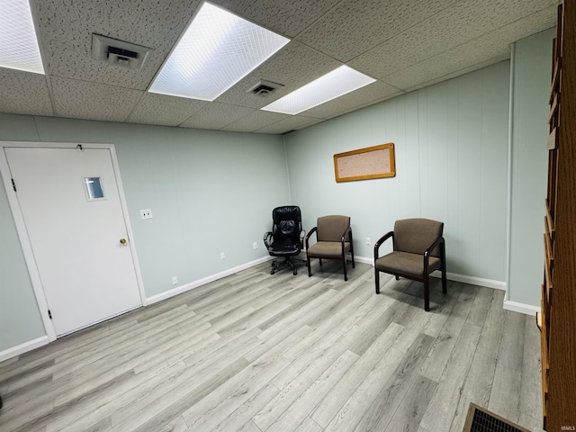 living area with light wood-style floors, a paneled ceiling, visible vents, and baseboards
