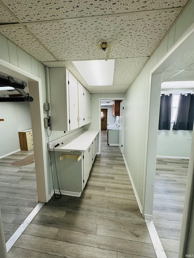hall with a paneled ceiling, light wood-style flooring, and baseboards