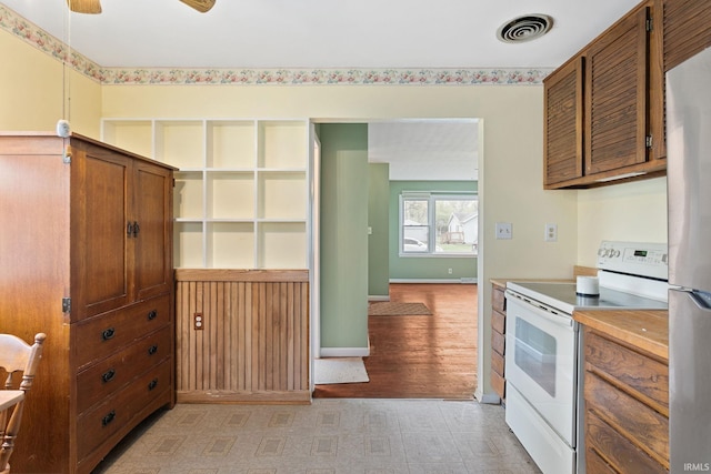 kitchen with freestanding refrigerator, brown cabinetry, electric range, baseboards, and visible vents
