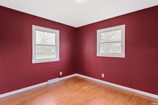 empty room featuring baseboards, visible vents, and light wood finished floors