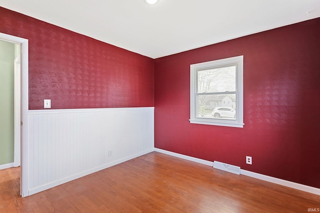 unfurnished room with visible vents, wainscoting, wood finished floors, and baseboards