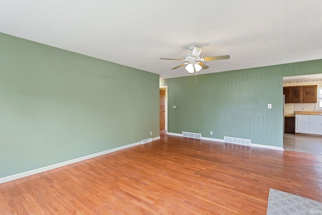 empty room featuring visible vents, a ceiling fan, light wood-style flooring, and baseboards