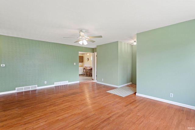 spare room with baseboards, visible vents, wood finished floors, and ceiling fan