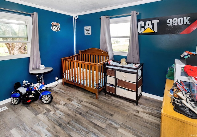 bedroom featuring baseboards, a crib, wood finished floors, and multiple windows