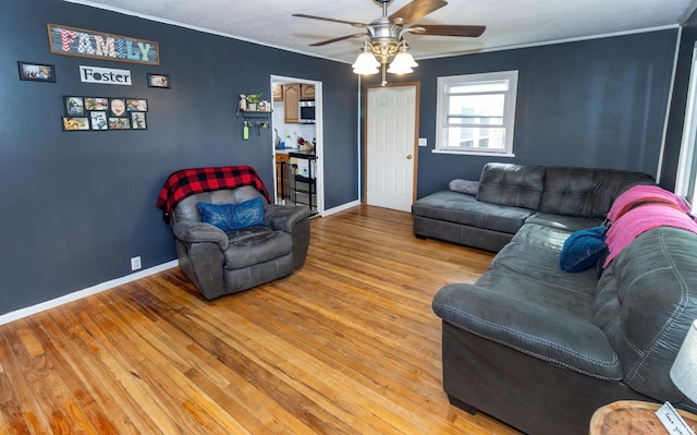 living area with baseboards, wood finished floors, a ceiling fan, and crown molding