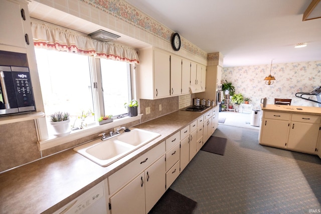 kitchen featuring a sink, stainless steel appliances, cream cabinets, light countertops, and wallpapered walls