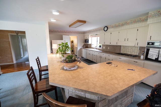 kitchen with white cabinetry, wallpapered walls, appliances with stainless steel finishes, and a kitchen bar