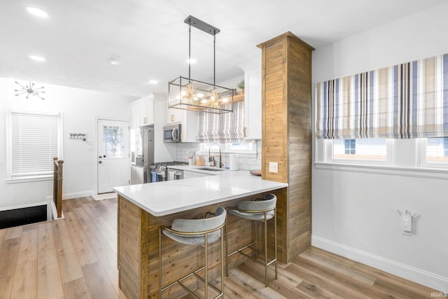 kitchen featuring a chandelier, stainless steel appliances, light countertops, light wood-type flooring, and baseboards