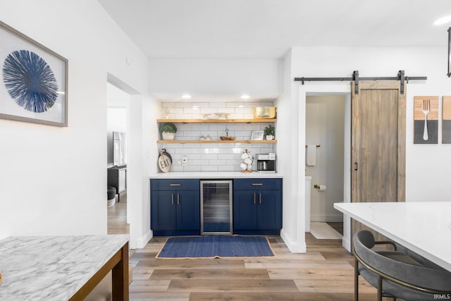 bar featuring light wood finished floors, a barn door, decorative backsplash, a dry bar, and beverage cooler