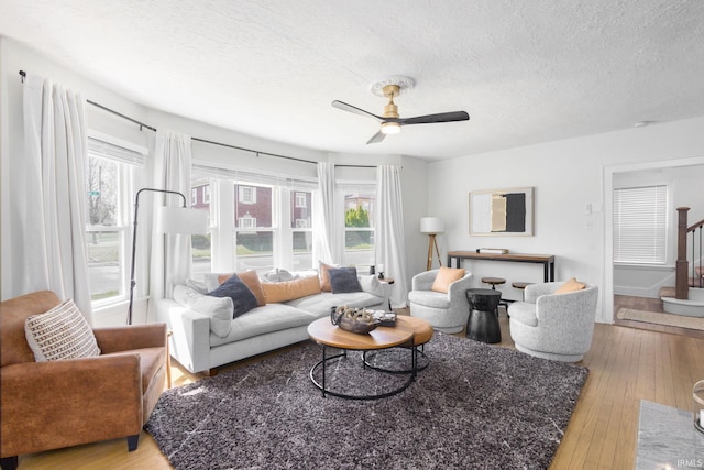 living area with stairs, a ceiling fan, a textured ceiling, and wood-type flooring