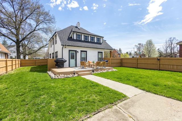 back of property with a deck, a chimney, stucco siding, a lawn, and a fenced backyard