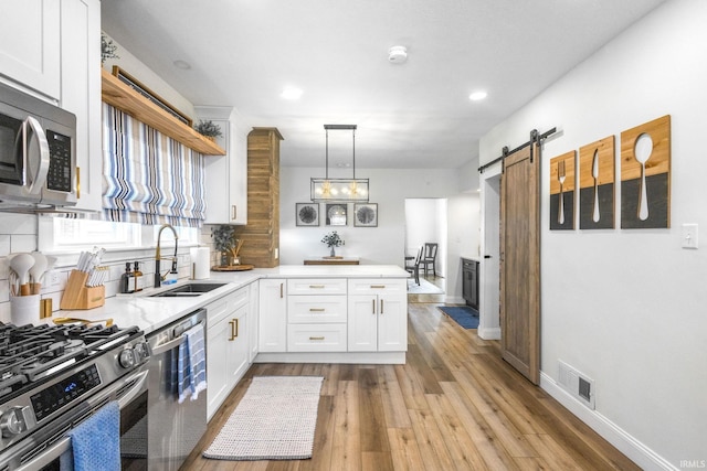 kitchen featuring a sink, a barn door, a peninsula, white cabinets, and appliances with stainless steel finishes