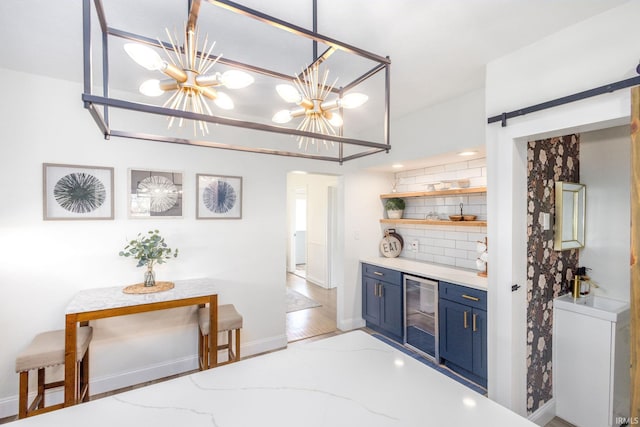 bar with wine cooler, baseboards, a chandelier, and backsplash