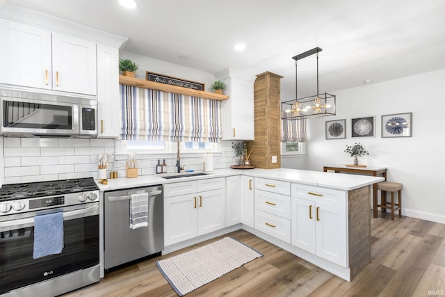 kitchen with a sink, decorative backsplash, a peninsula, white cabinets, and appliances with stainless steel finishes