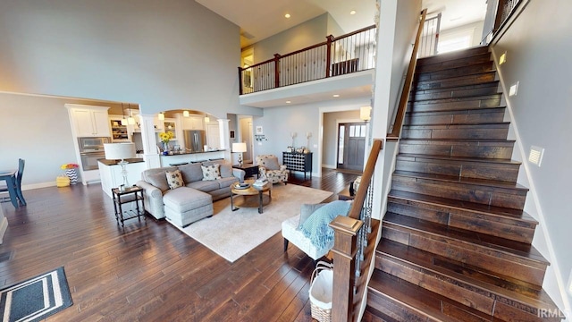 living area featuring dark wood-style floors, decorative columns, baseboards, a towering ceiling, and arched walkways