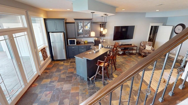 kitchen with glass insert cabinets, a breakfast bar, recessed lighting, and freestanding refrigerator