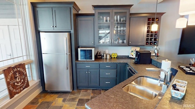 bar with hanging light fixtures, freestanding refrigerator, stone finish floor, a sink, and indoor bar