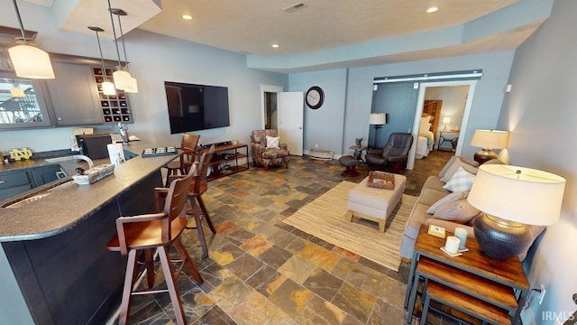 living room featuring a barn door, visible vents, stone tile flooring, and recessed lighting