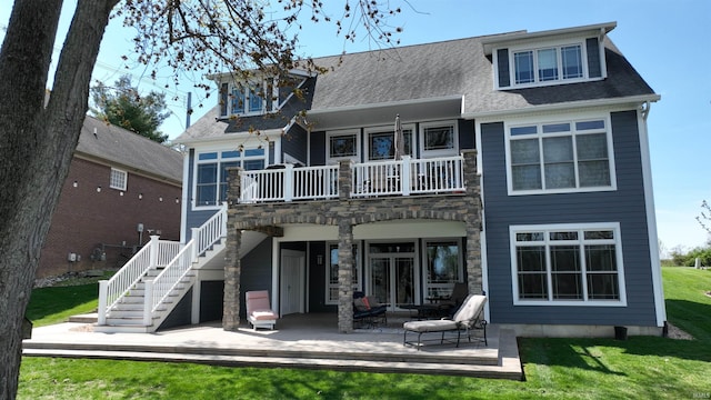 back of house featuring a balcony, a patio, stone siding, a lawn, and stairway