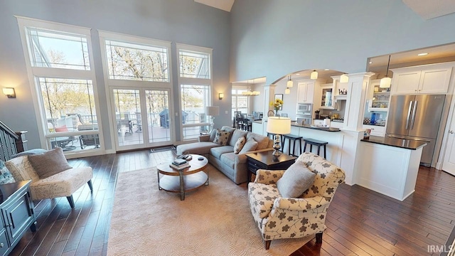 living area with dark wood-style floors, decorative columns, arched walkways, and a towering ceiling