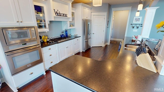 kitchen featuring decorative light fixtures, appliances with stainless steel finishes, dark countertops, a sink, and white cabinetry