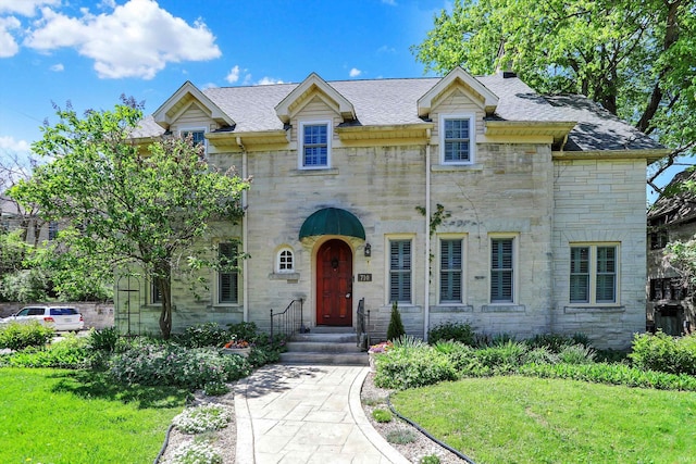 view of front of property featuring a front yard, a shingled roof, and stone siding