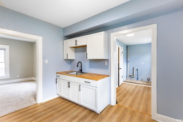 kitchen featuring light wood-style flooring, wood counters, white cabinets, a sink, and baseboards