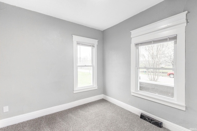 carpeted empty room featuring a wealth of natural light, visible vents, and baseboards